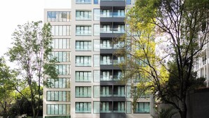 A multi-story residential building with large windows, balconies, and a well-maintained surrounding area with trees and shrubs. - Crisol Suites Condesa (Mexico City)