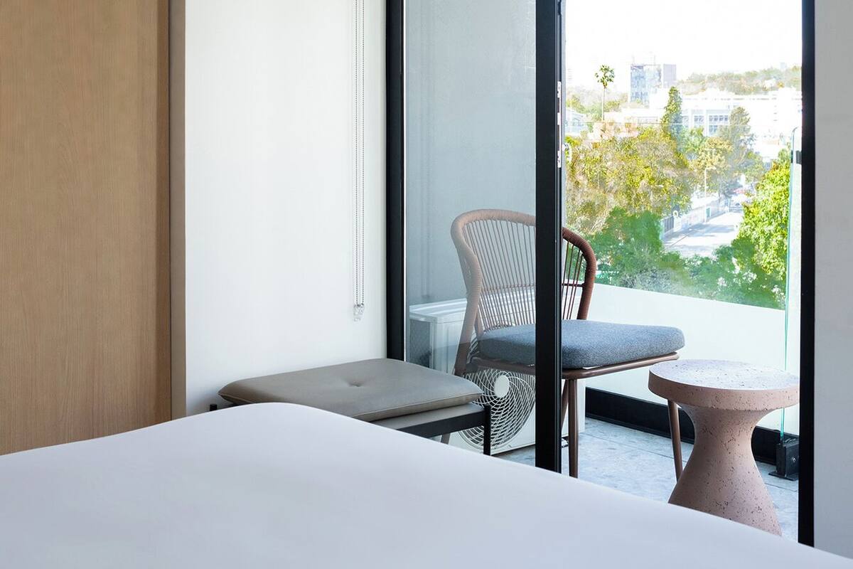 Une chambre d’hôtel avec un lit, une chaise, une petite table et un balcon donnant sur la ville.