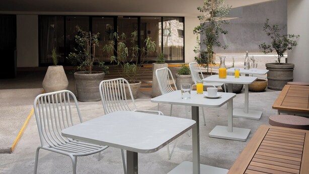 An outdoor patio area with white metal chairs and tables, potted plants, and a view of the street. - Crisol Suites Condesa (Mexico City)