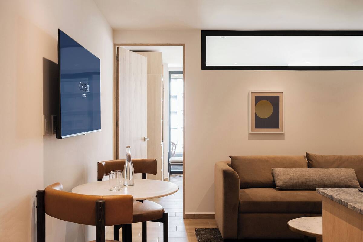 Un salon moderne avec un canapé en cuir marron, une table basse ronde et un coin repas comprenant une petite table et des chaises.