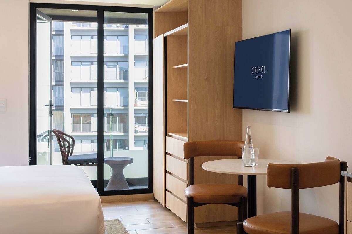 Une chambre d’hôtel avec un lit, une télévision, une petite table avec des chaises et une vue sur la ville grâce à de grandes fenêtres.