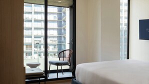 A hotel room with a bed, a chair, and a view of a high-rise building. - Crisol Suites Condesa (Mexico City)