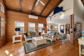 A spacious living room with wooden floors, a high ceiling, and a large fish mounted on the wall.