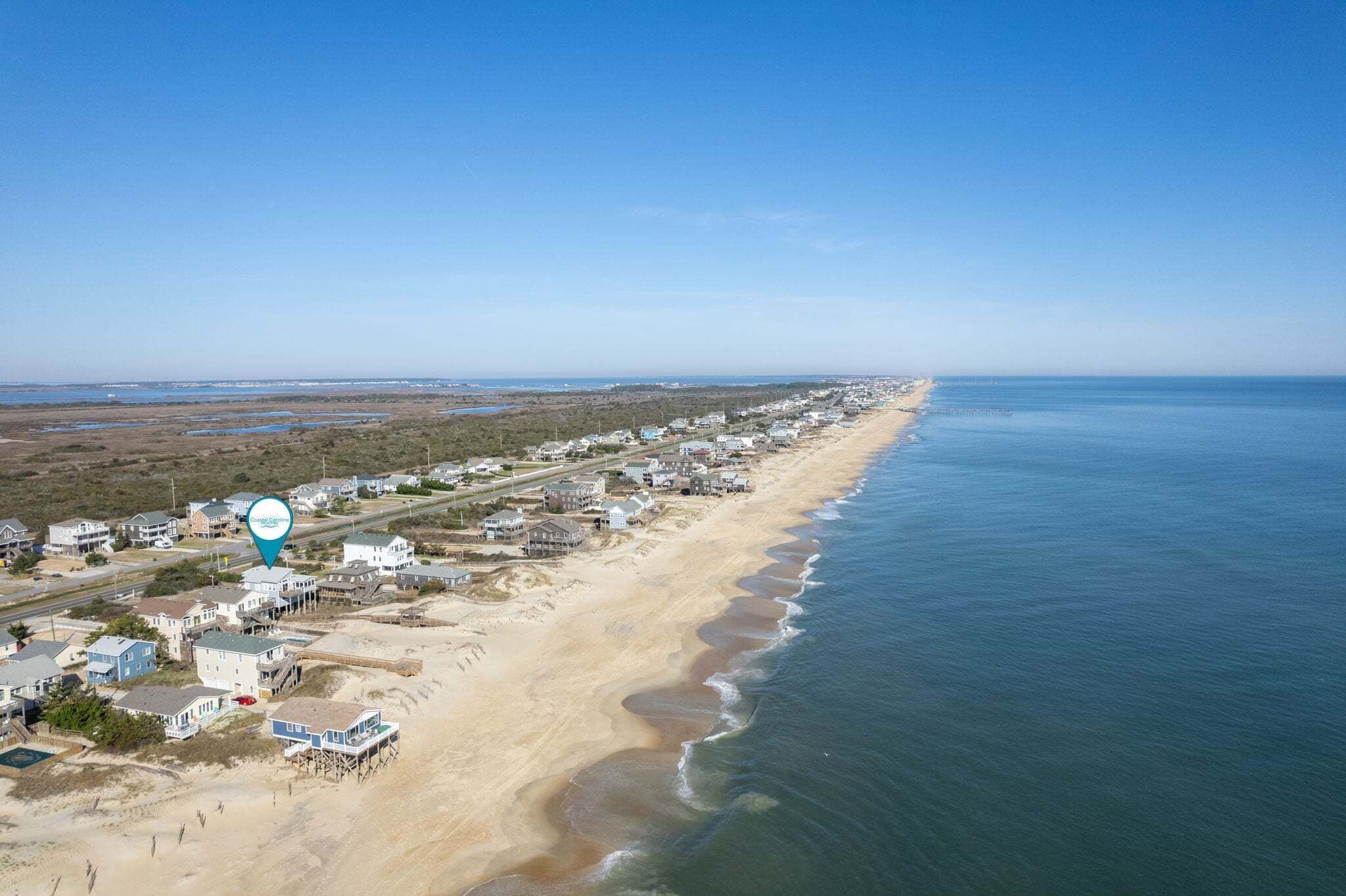 Vista aérea de una zona residencial costera con casas a lo largo de la playa y cielo despejado.