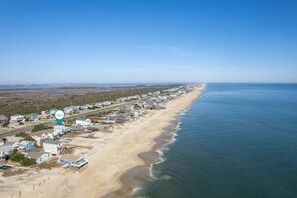 An aerial view of a coastal residential area with houses along the beach and a clear sky. - Moonshadow: Oceanfront, walkway to the beach, hot tub, awesome ocean views! (Nags Head)