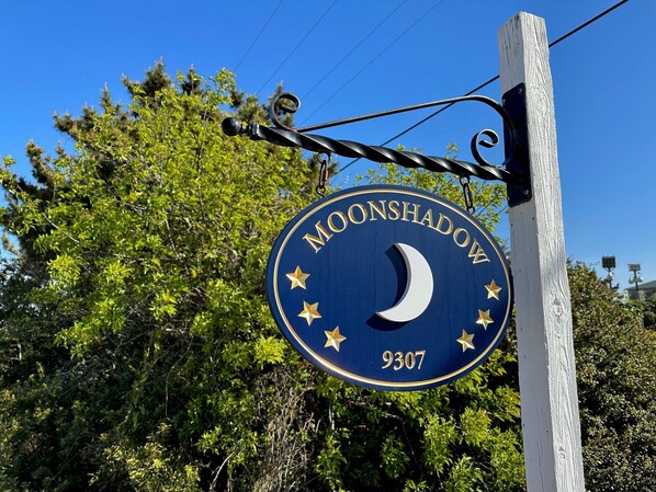 A sign with the text "MOONSHADOW" and the number "9307" against a backdrop of trees and a clear sky.