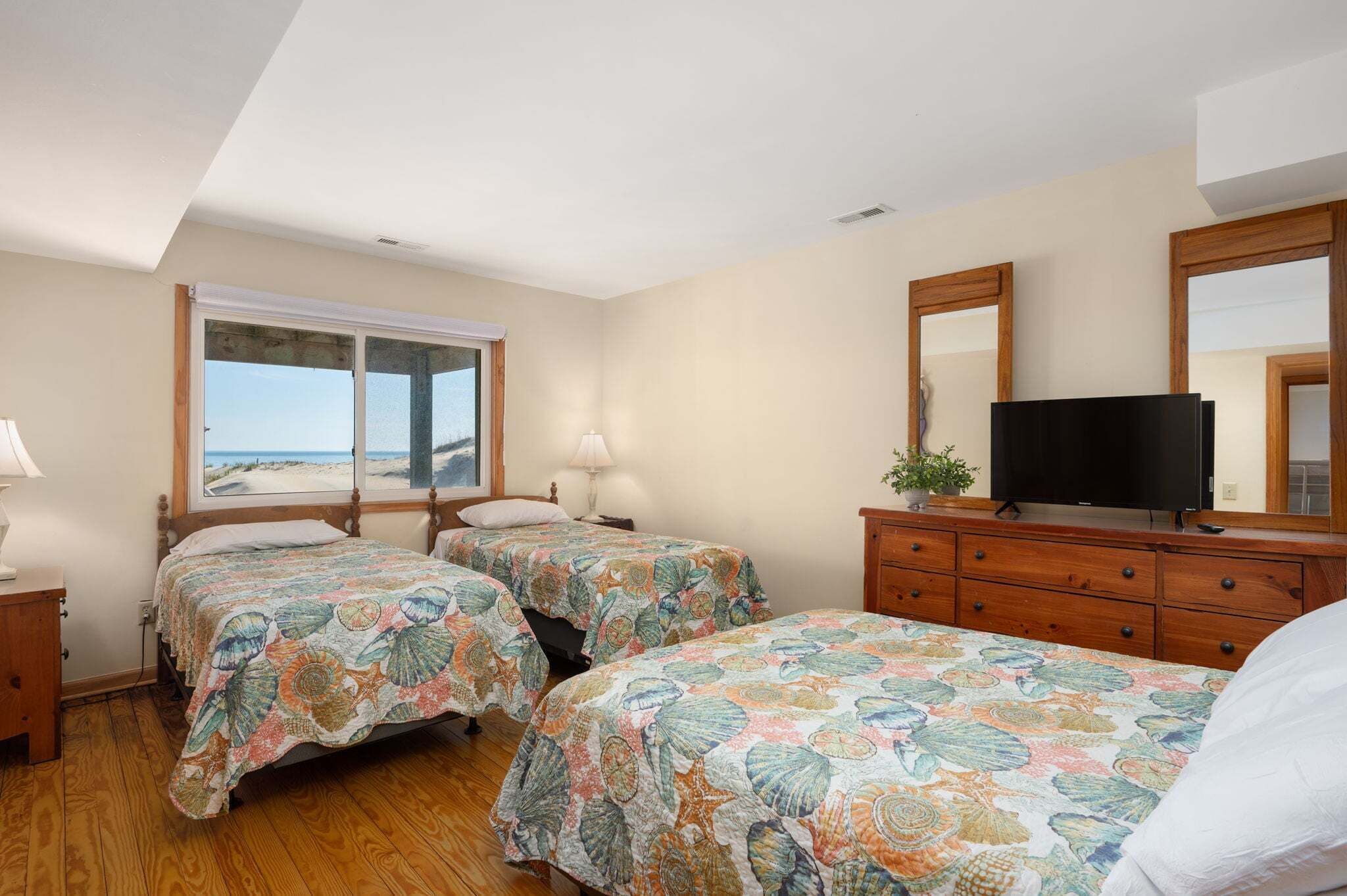 Une chambre avec deux lits, une télévision, une commode et une fenêtre donnant sur la plage.