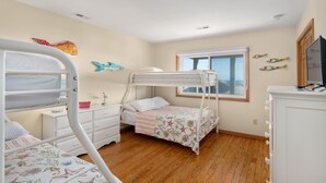 A child’s bedroom with bunk beds, a dresser, a desk, and a window with a view. - Moonshadow: Oceanfront, walkway to the beach, hot tub, awesome ocean views! (Nags Head)