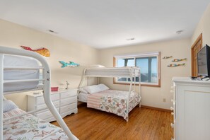 A child’s bedroom with bunk beds, a dresser, a desk, and a window with a view.