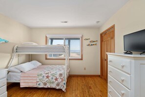 A bedroom with bunk beds, a television, a dresser, and a window with a view.