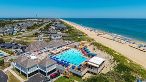 A coastal resort with a large swimming pool, beach access, and residential buildings. - Moonshadow: Oceanfront, walkway to the beach, hot tub, awesome ocean views! (Nags Head)