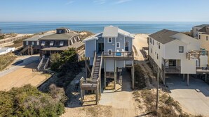 A beachfront property with multiple houses, a wooden staircase leading to a deck, and a clear view of the ocean. - Moonshadow: Oceanfront, walkway to the beach, hot tub, awesome ocean views! (Nags Head)