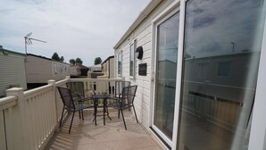 A covered outdoor patio with a table and chairs, a white fence, and a sliding glass door. - 3 Bedroom Caravan Pets Free Linen Included (King's Lynn)