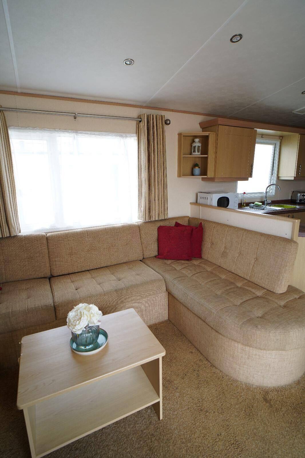 A compact living space with a sofa, a small table, a kitchen area, and a window with curtains.