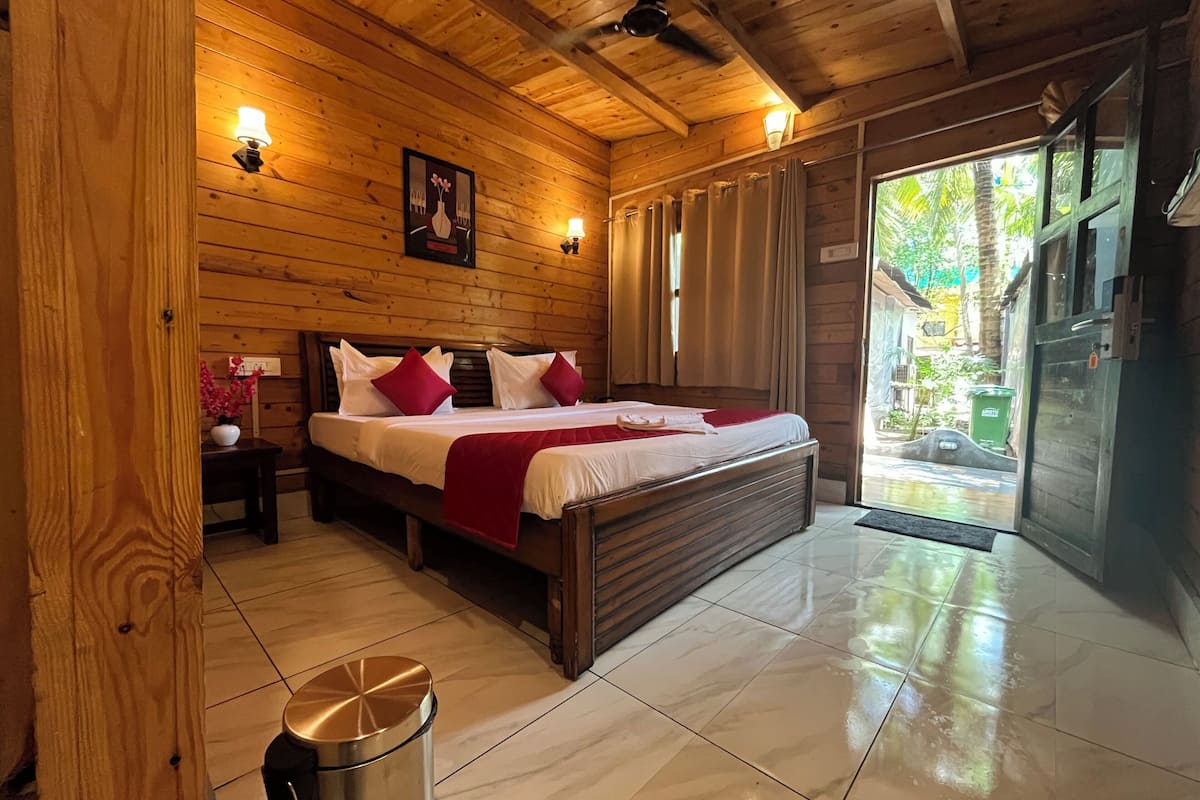 Quarto com painéis de madeira, uma cama grande, duas luminárias de cabeceira, um quadro na parede e vista exterior por uma porta de vidro.