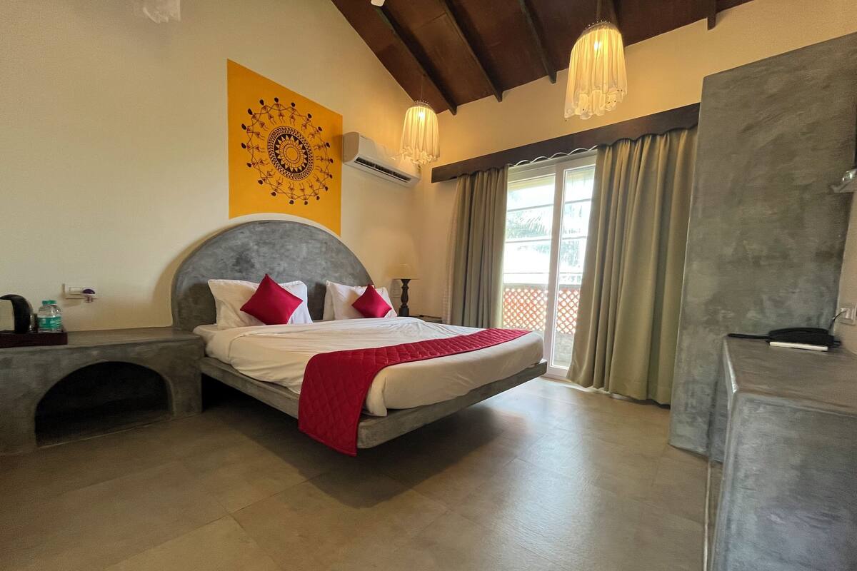 Quarto com cama, cabeceira, ar condicionado fixado na parede, janela com cortinas e vista para o exterior.