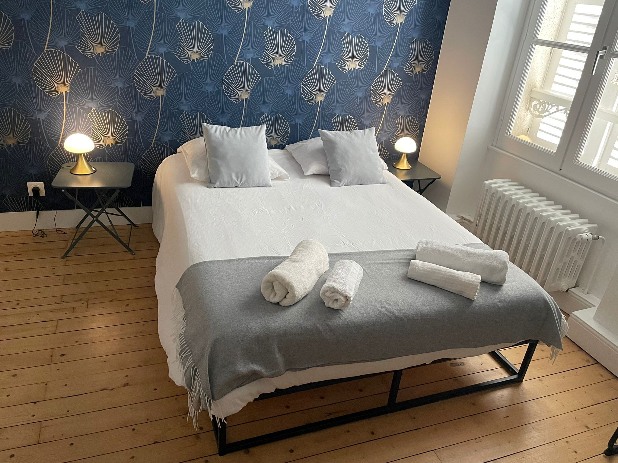 Una cama bien hecha con almohadas y toallas, una mesita con una lámpara y un radiador.
