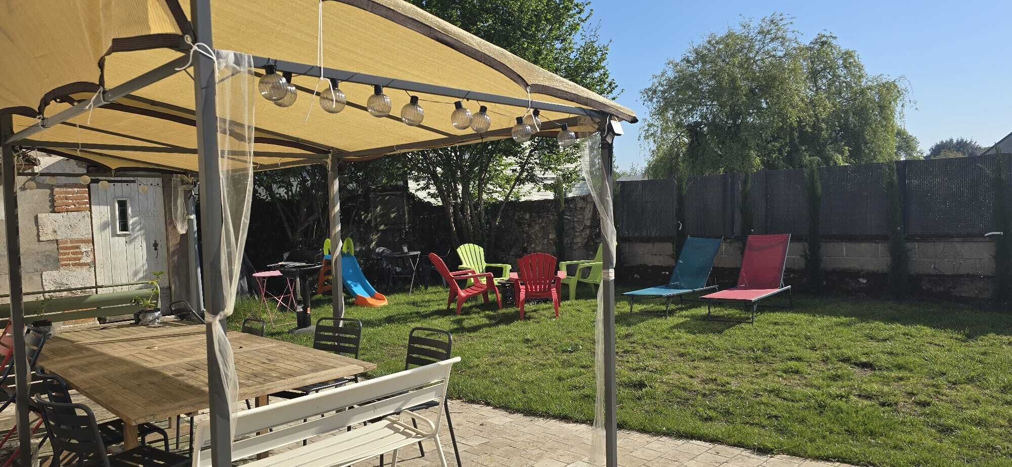 A backyard with a covered patio, a slide, and colorful chairs.