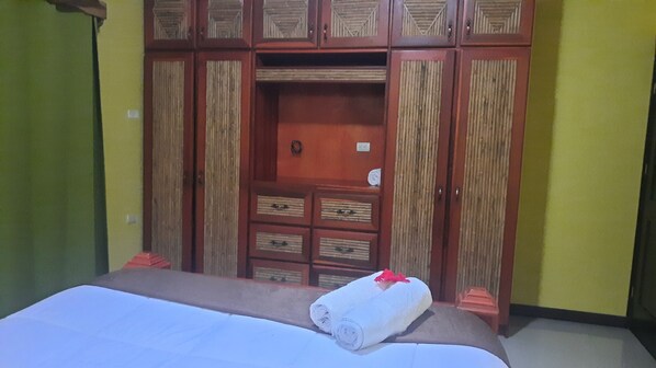 A hotel room with a bed, a wooden wardrobe with multiple compartments, and a small table.
