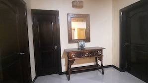 Un pasillo con dos puertas de madera oscura, una pequeña consola de madera con un espejo encima, y un suelo de tonos claros.