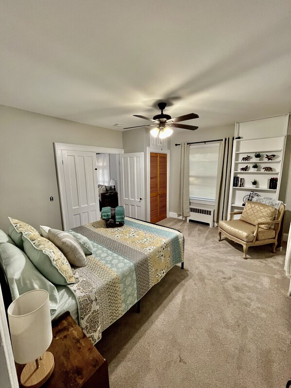 A bedroom with a bed, a chair, a ceiling fan, and a bookshelf.