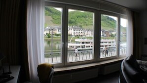 Quarto com uma grande janela com vista para um rio, uma cadeira e uma mesa.