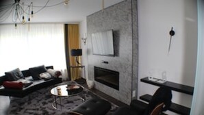 Uma sala de estar moderna com lareira, um conjunto de sofás, uma mesa de centro e uma TV fixada na parede.
