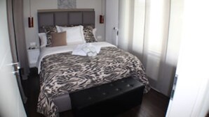 Quarto com cama grande, cabeceira, mesa de cabeceira e janela com cortinas.