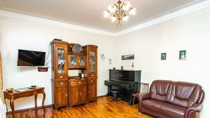 Un salon avec un plancher en bois, un canapé en cuir marron, une armoire en bois, un téléviseur et un lustre.