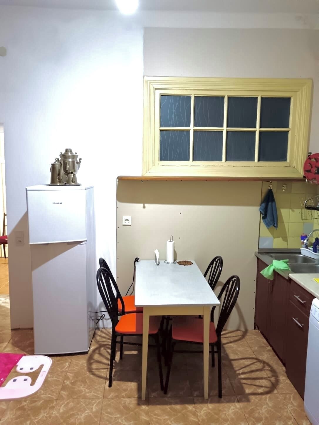 Cuina compacta amb taula de menjador, cadira, nevera i finestra sobre l'evador.