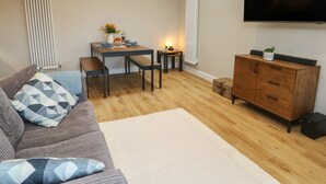 Un salon moderne comprenant un canapé, une table à manger avec des bancs, un téléviseur fixé au mur et un meuble en bois.
