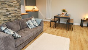 Un salon moderne avec un canapé gris, un tapis blanc, une table à manger avec des chaises et un coin cuisine avec un radiateur blanc.