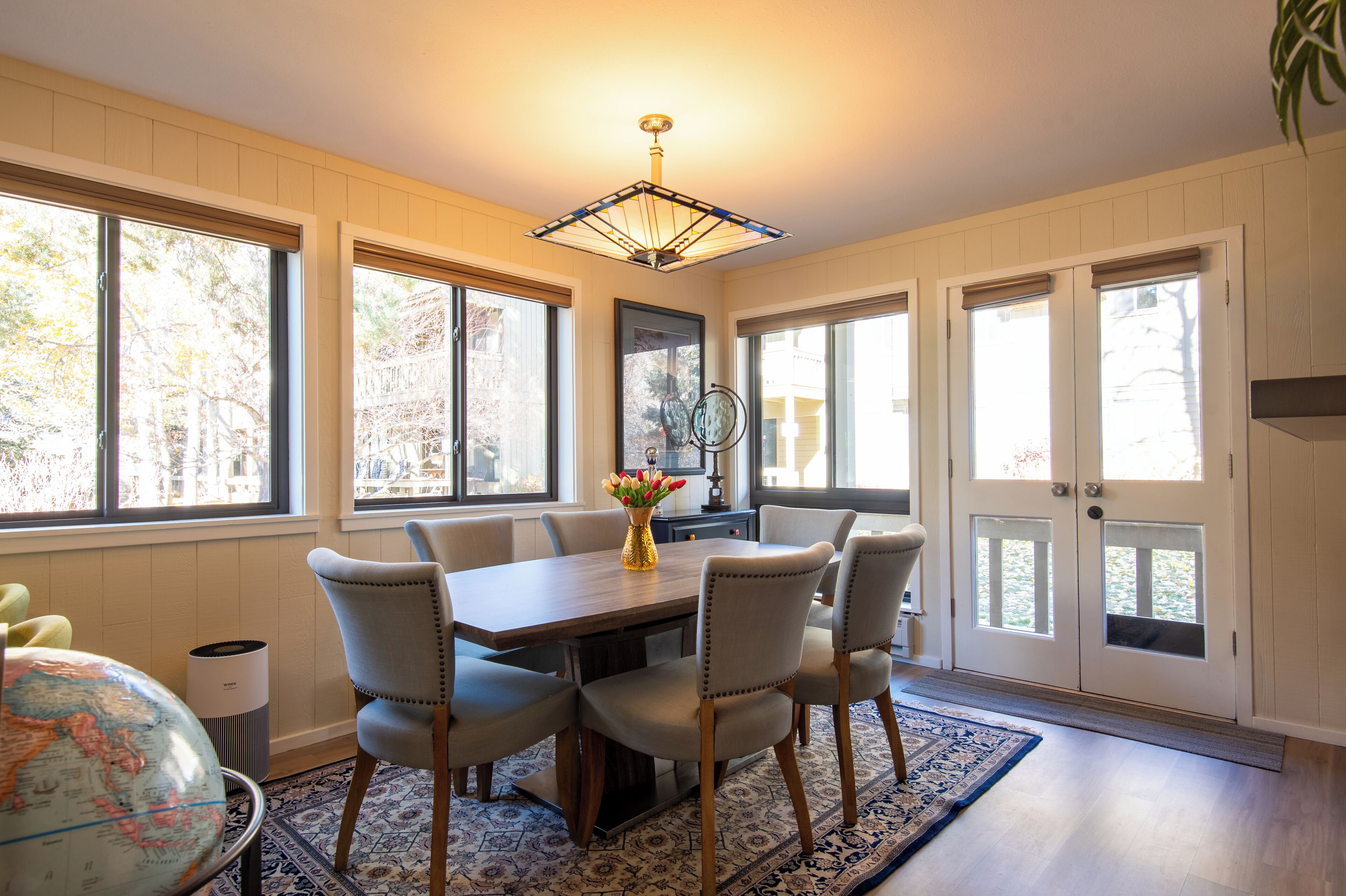 A dining area with a wooden table, four chairs, a globe, and a vase with flowers.
