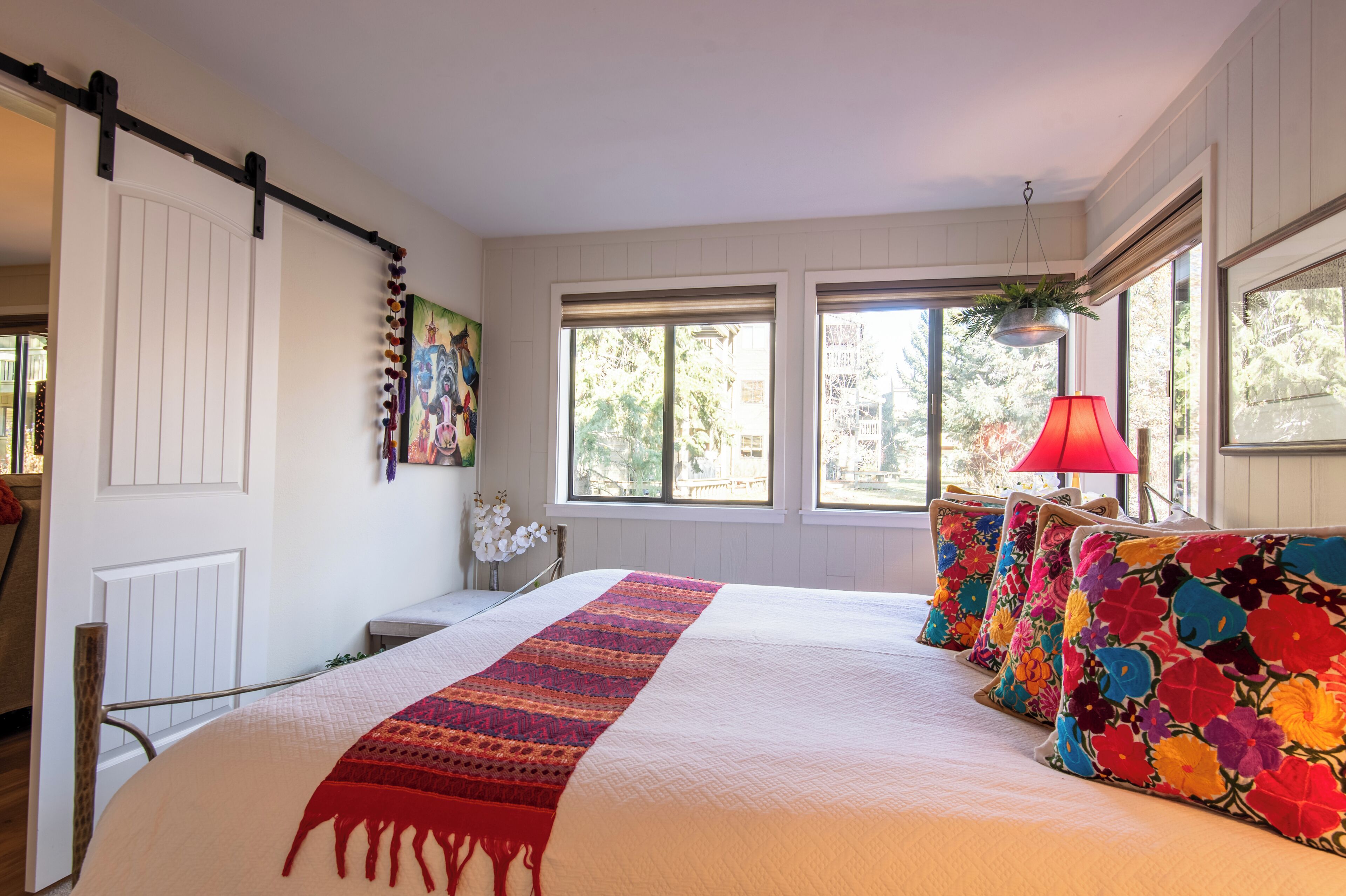 A bedroom with a large bed, a red lamp, and a window with a view of trees.