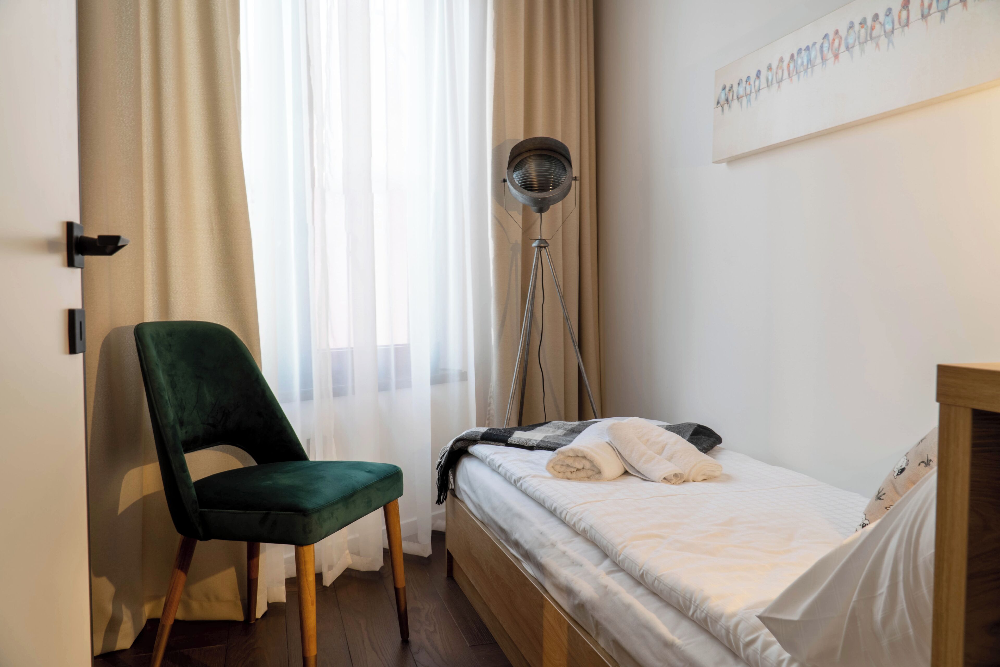 Ein Schlafzimmer mit einem Bett, einem Sessel, einer Stehlampe und einem Fenster mit Vorhängen.
