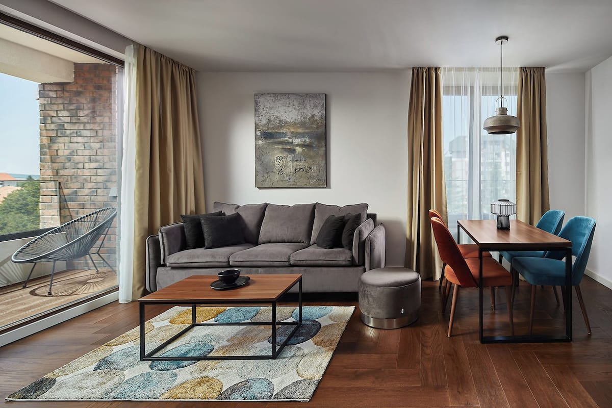 A modern living room with a grey sofa, a wooden coffee table, a dining table with chairs, and a hanging light fixture.