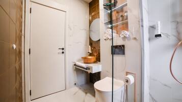 A bathroom with a white door, a copper sink, a toilet, and a glass shower enclosure.