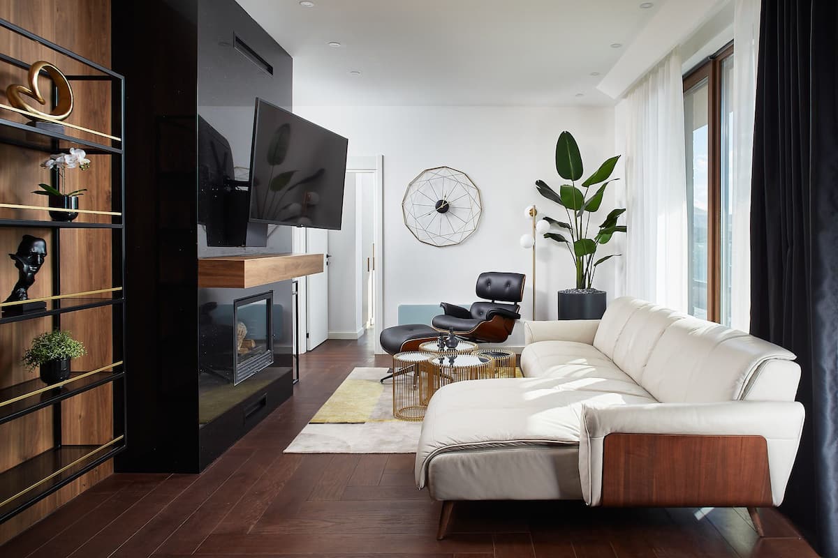 A modern living room with a white sofa, a flat-screen TV, a wooden bookshelf, and a large window with curtains.