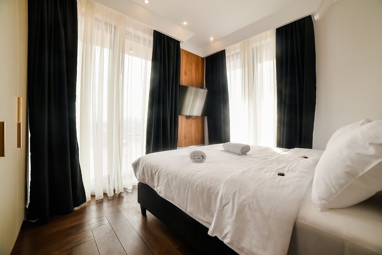 Una camera d'albergo moderna con un grande letto, tende bianche e nere, un pannello di legno sulla parete e un lampadario a soffitto.