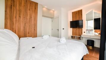 A modern hotel room with a wooden headboard, a flat-screen TV, a bedside table, and a large mirror.