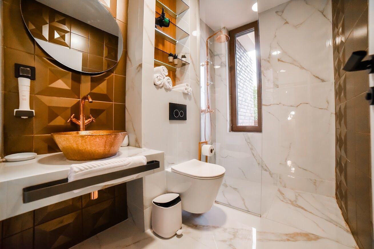 A modern bathroom with a large copper basin, a toilet, and a glass-enclosed shower.