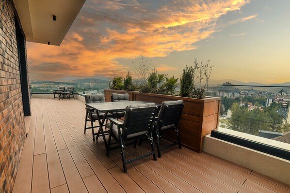 A rooftop terrace with a wooden deck, a table with chairs, and a view of the cityscape during sunset. - 21 Century Zlatibor by Adora (Zlatibor)