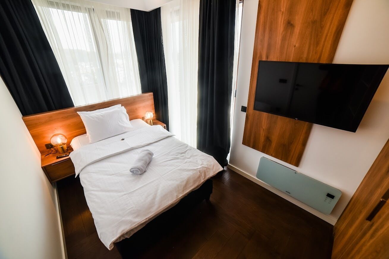 Une chambre d’hôtel avec un lit, des lampes de chevet, un téléviseur à écran plat fixé au mur et un plancher en bois.