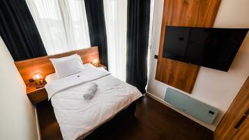 Une chambre d’hôtel avec un lit, des lampes de chevet, un téléviseur à écran plat fixé au mur et un plancher en bois.