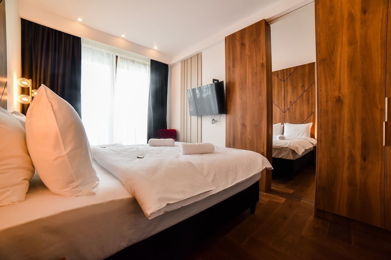 A hotel room with a large bed, a TV mounted on the wall, and a wooden wardrobe.