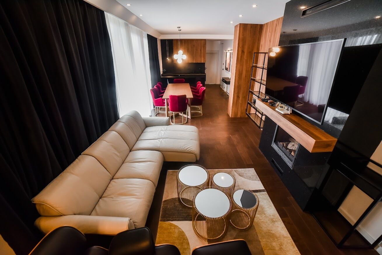 A modern living room with a sectional sofa, a dining area with red chairs, a flat-screen TV, and a fireplace.