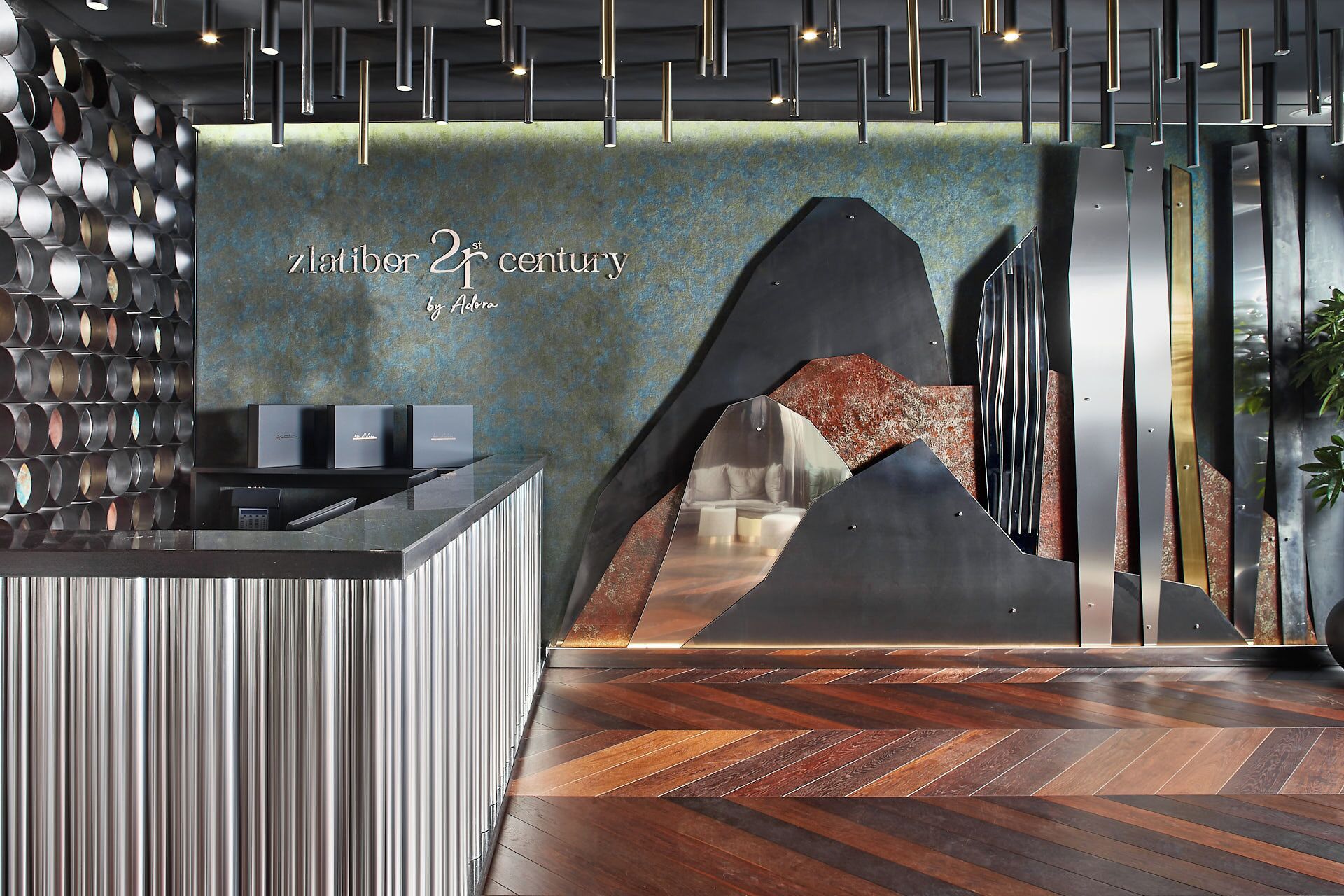 A modern reception area with a herringbone wood floor, a wall-mounted cylindrical object, and a sign reading "7th century by Adora".