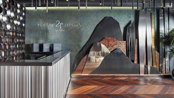 A modern reception area with a herringbone wood floor, a wall-mounted cylindrical object, and a sign reading "7th century by Adora".