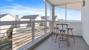 A balcony with a glass railing, a table with two stools, and a clear view of neighboring buildings and the sky. - Bona View G36 (Cape Town)
