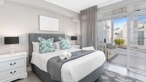 A modern bedroom with a large bed, two bedside tables, a nightstand, and a view of the outside through large sliding glass doors. - Bona View G36 (Cape Town)